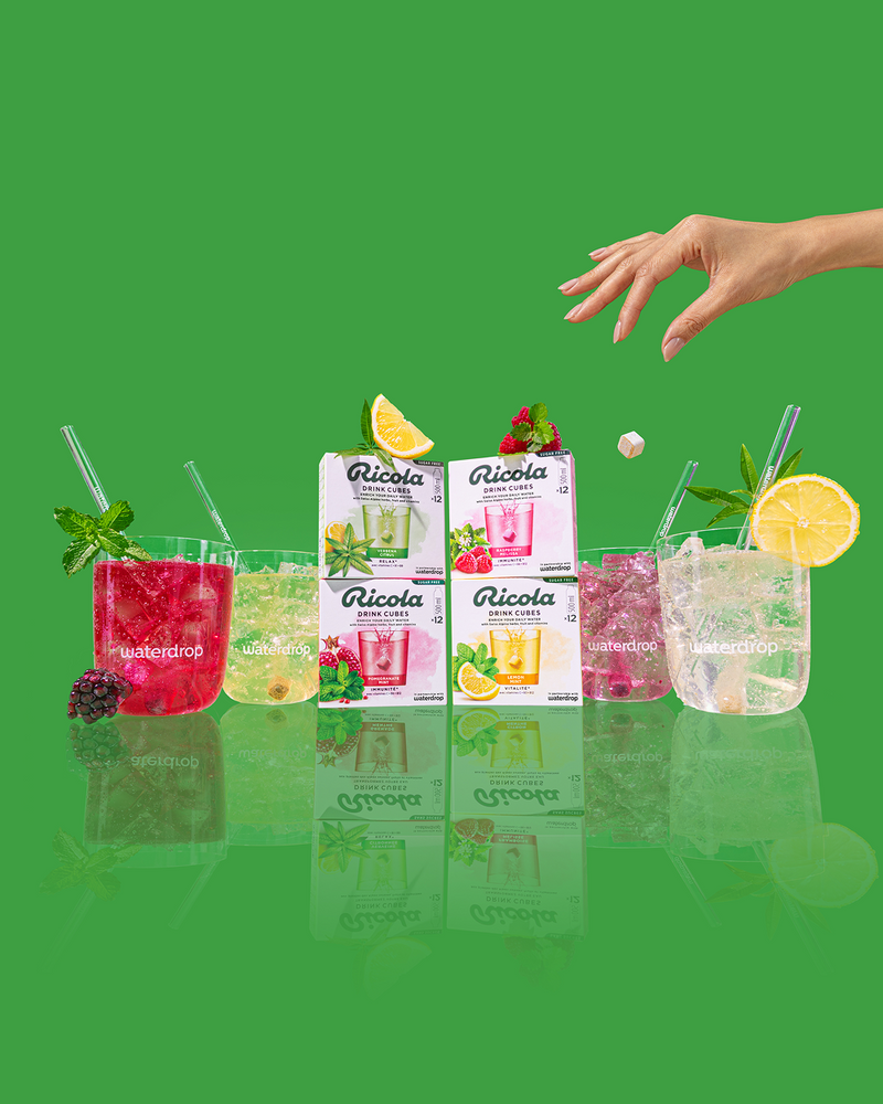 Ricola flavours in Glasses. A hand in the top right corner is dropping a drink cube into a glass.