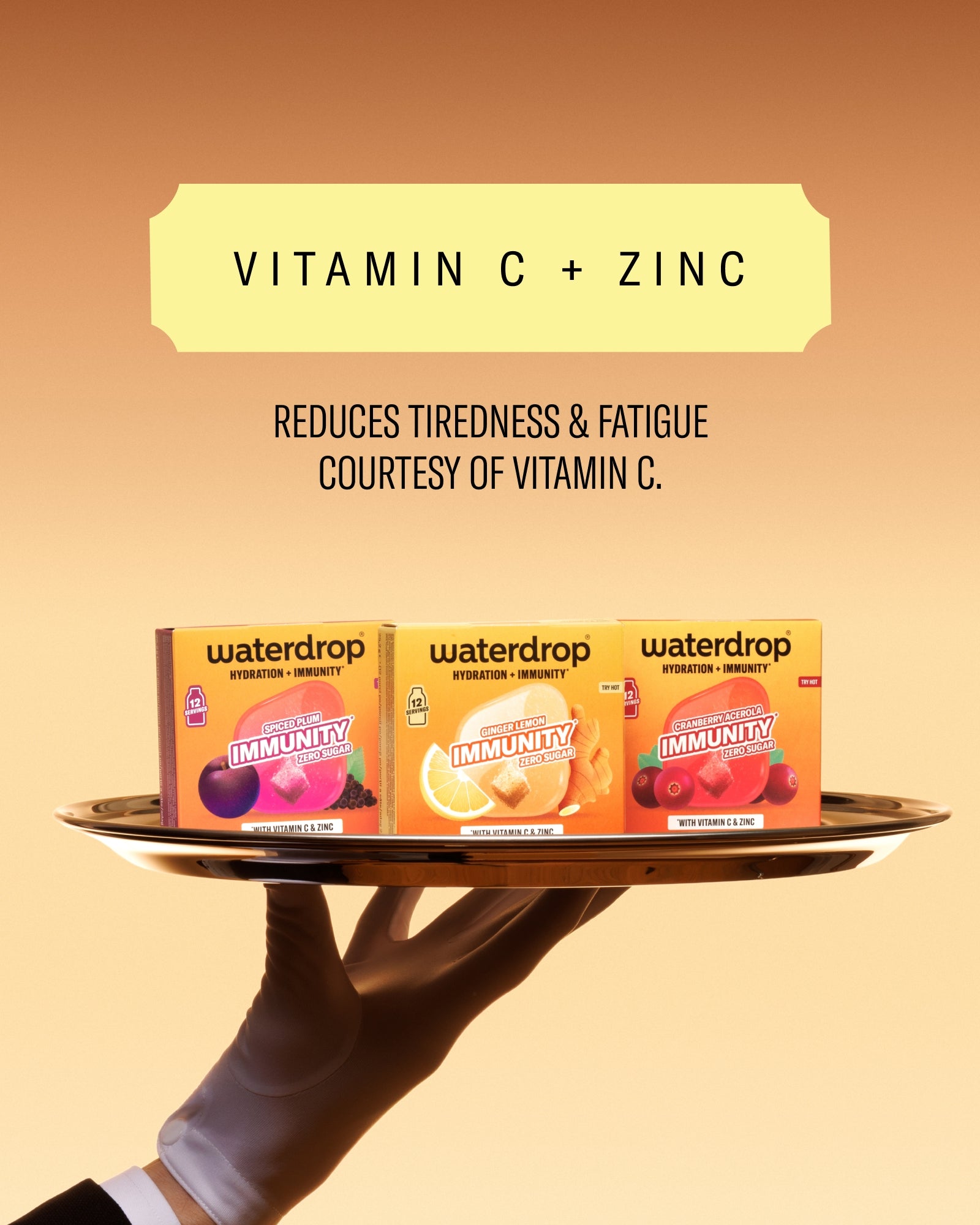 Tri kutije vitamina na okrugloj pladnji koju drži obučena ruka protiv narančaste pozadine s gradijentom.