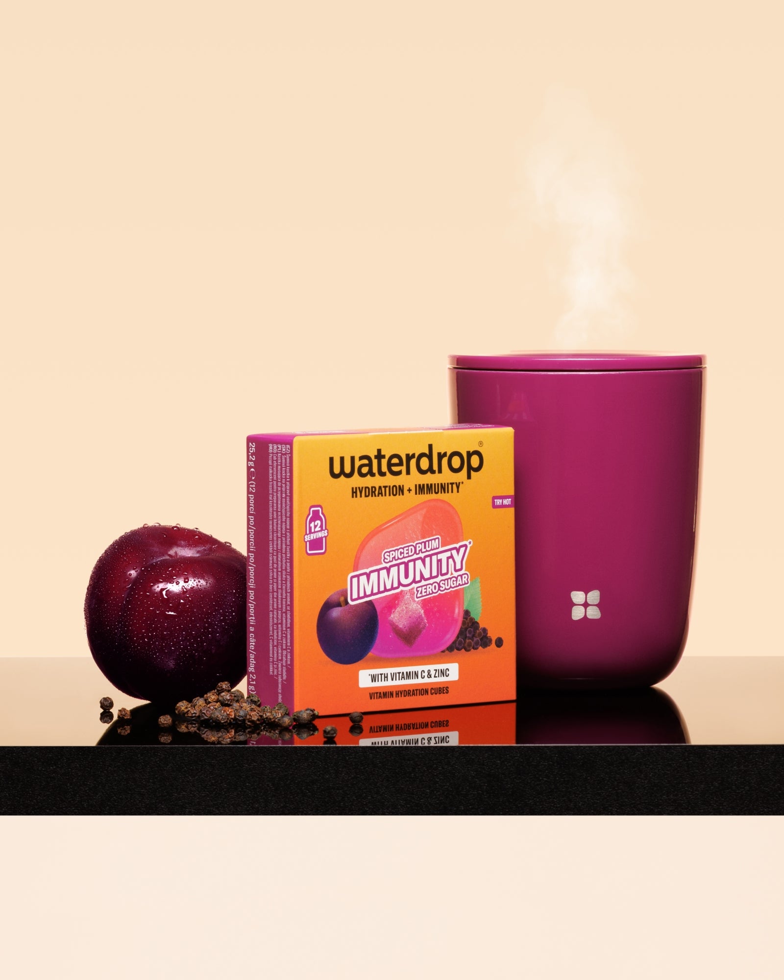 Kutija Waterdrop imunost otpora uz šljivu i ružičastu šalicu s parom na crnoj površini.